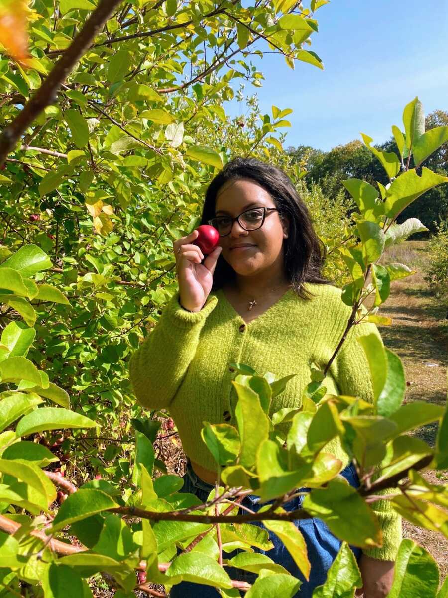 body positivity activist in green fuzzy shirt holding an apple in an orchard