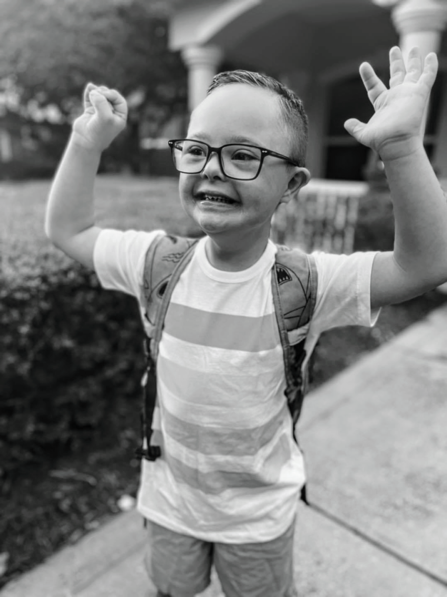 Boy with down syndrome stands outside with his arms in the air