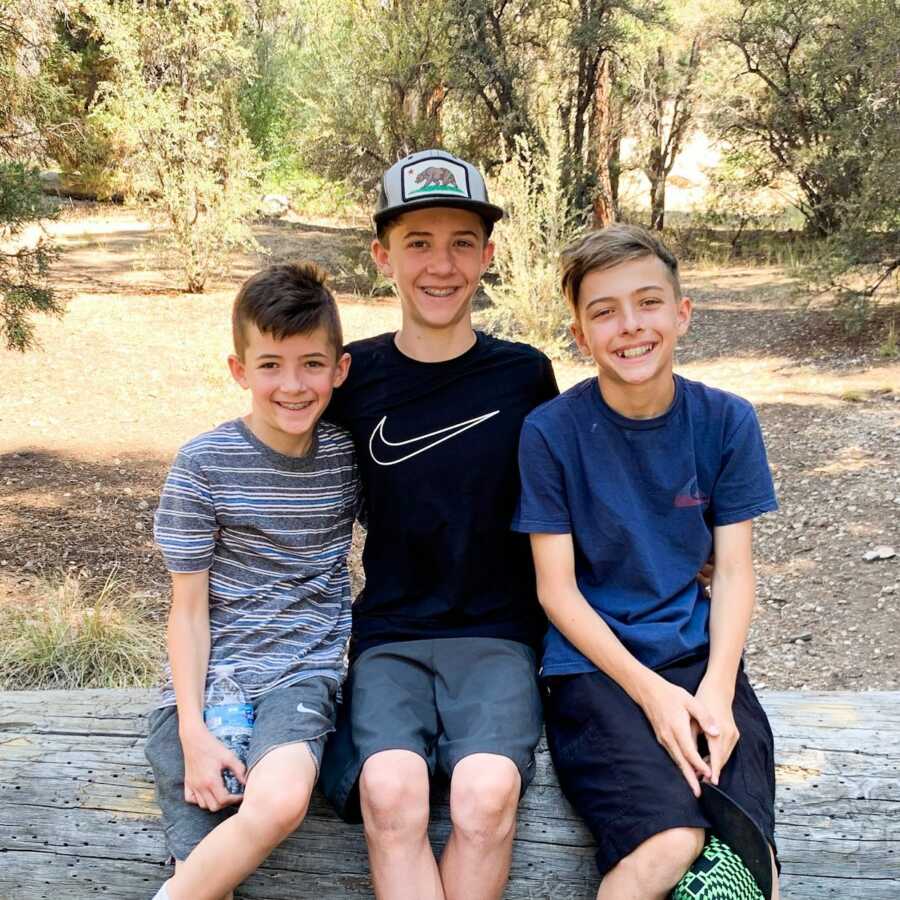 Brothers wearing basketball shorts and t-shirts sit on a fallen tree for a picture while hiking in California.