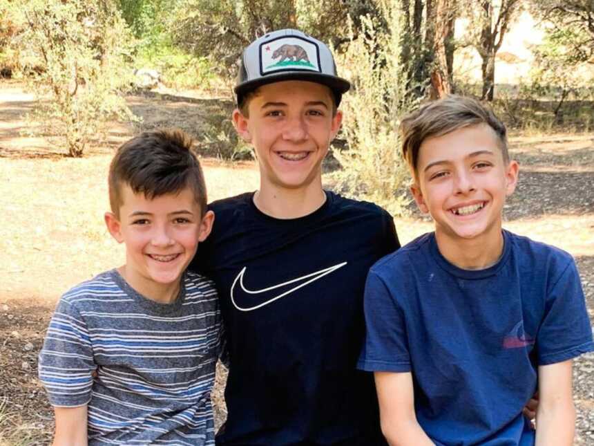 Close up of three brothers sitting together and smiling while resting on a hike.