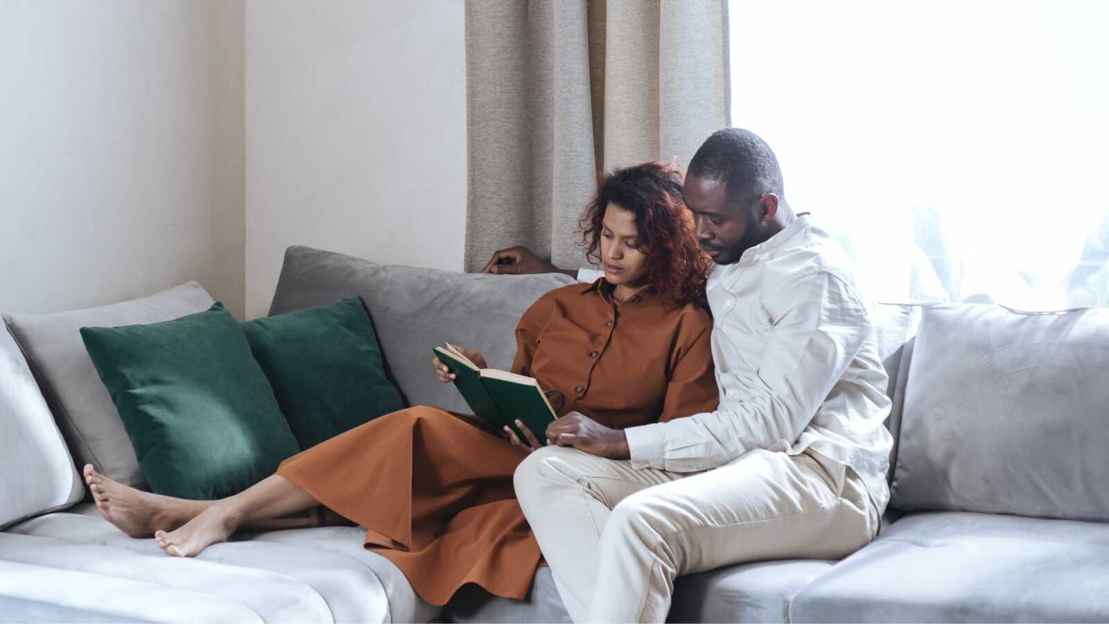 black couple sits on couch together while woman holds book they're reading