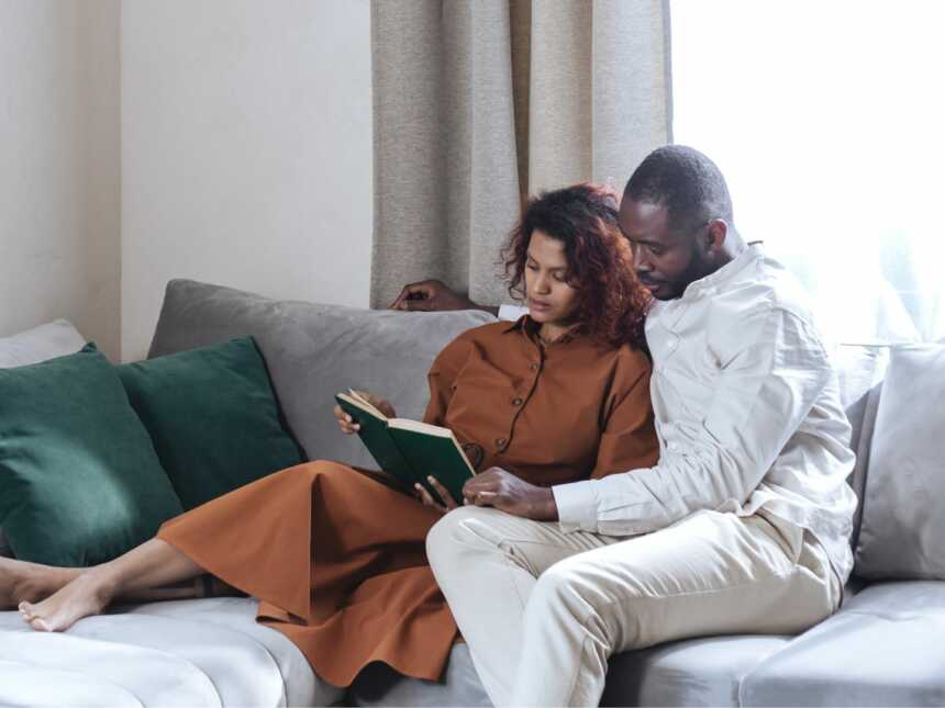 black couple sits on couch together while woman holds book they're reading