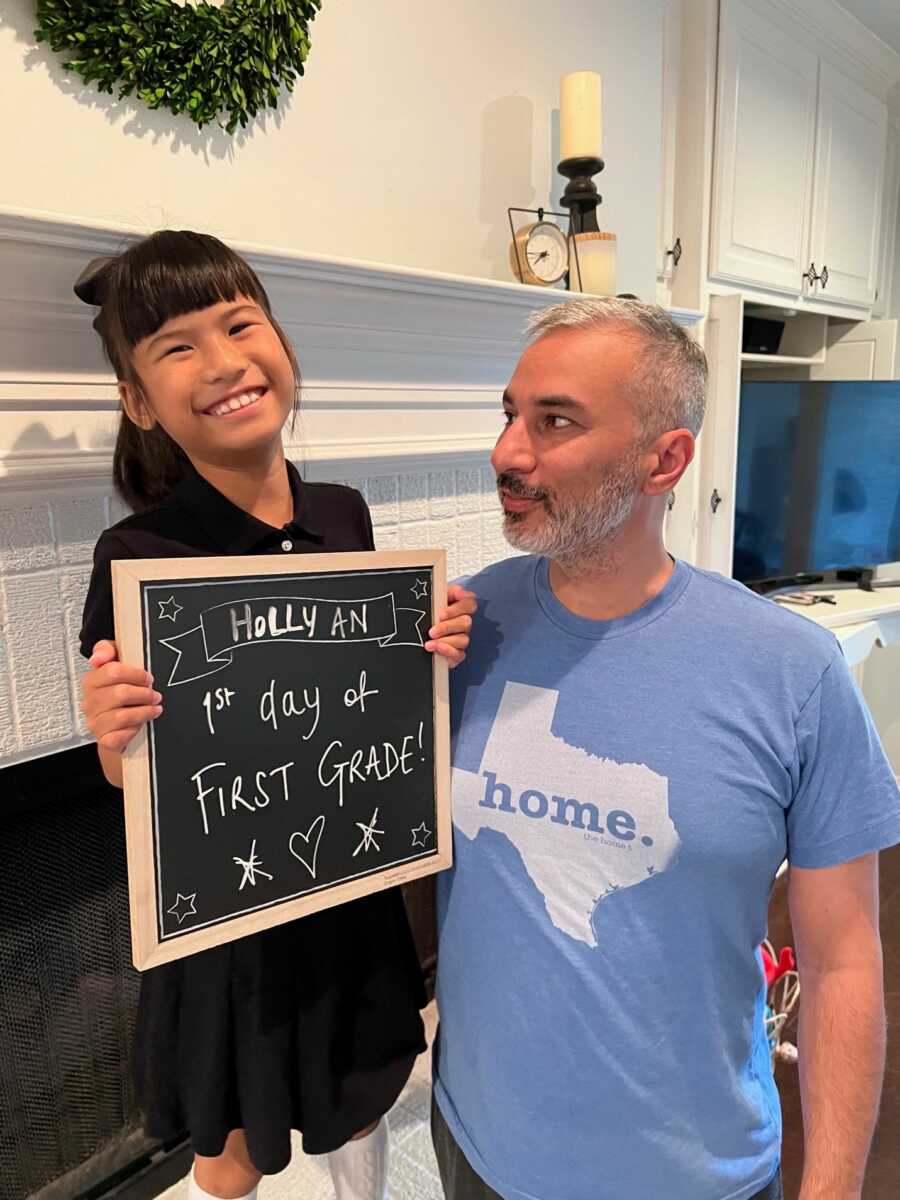 Adoptive father with internationally adopted daughter holding first day of school sign