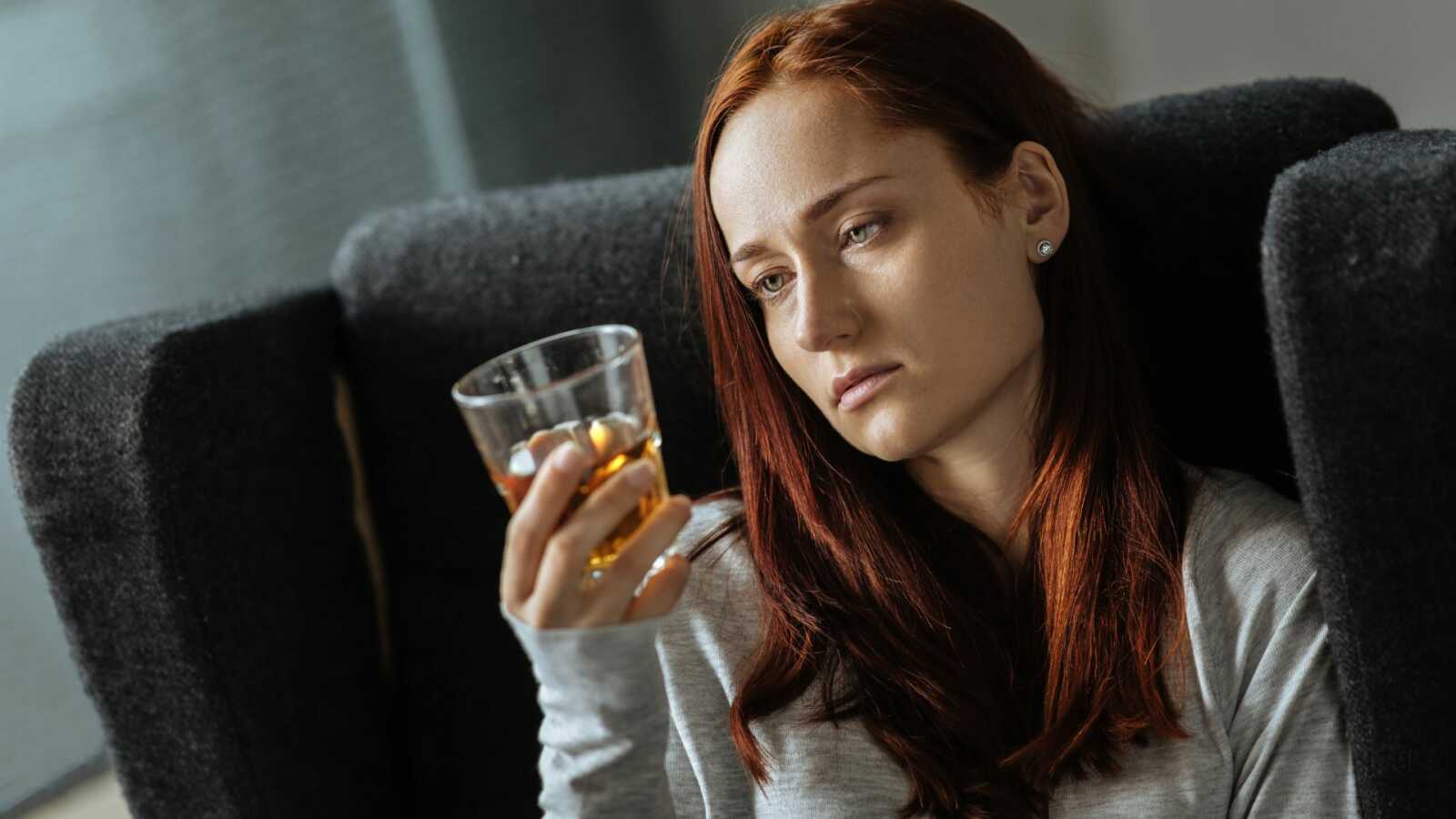 depressed woman holds up glass of alcohol and stares at it