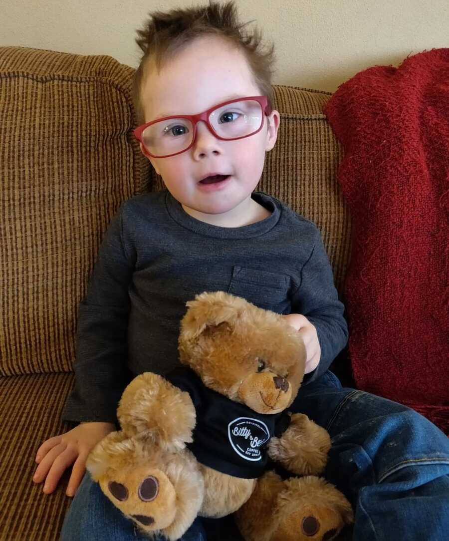 toddler with down syndrome sits holding teddy bear