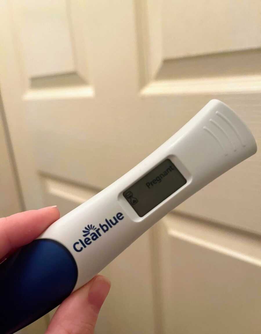 fingers holding a positive pregnancy test