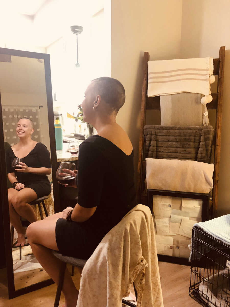 Cancer survivor smiles into mirror with her shaved head