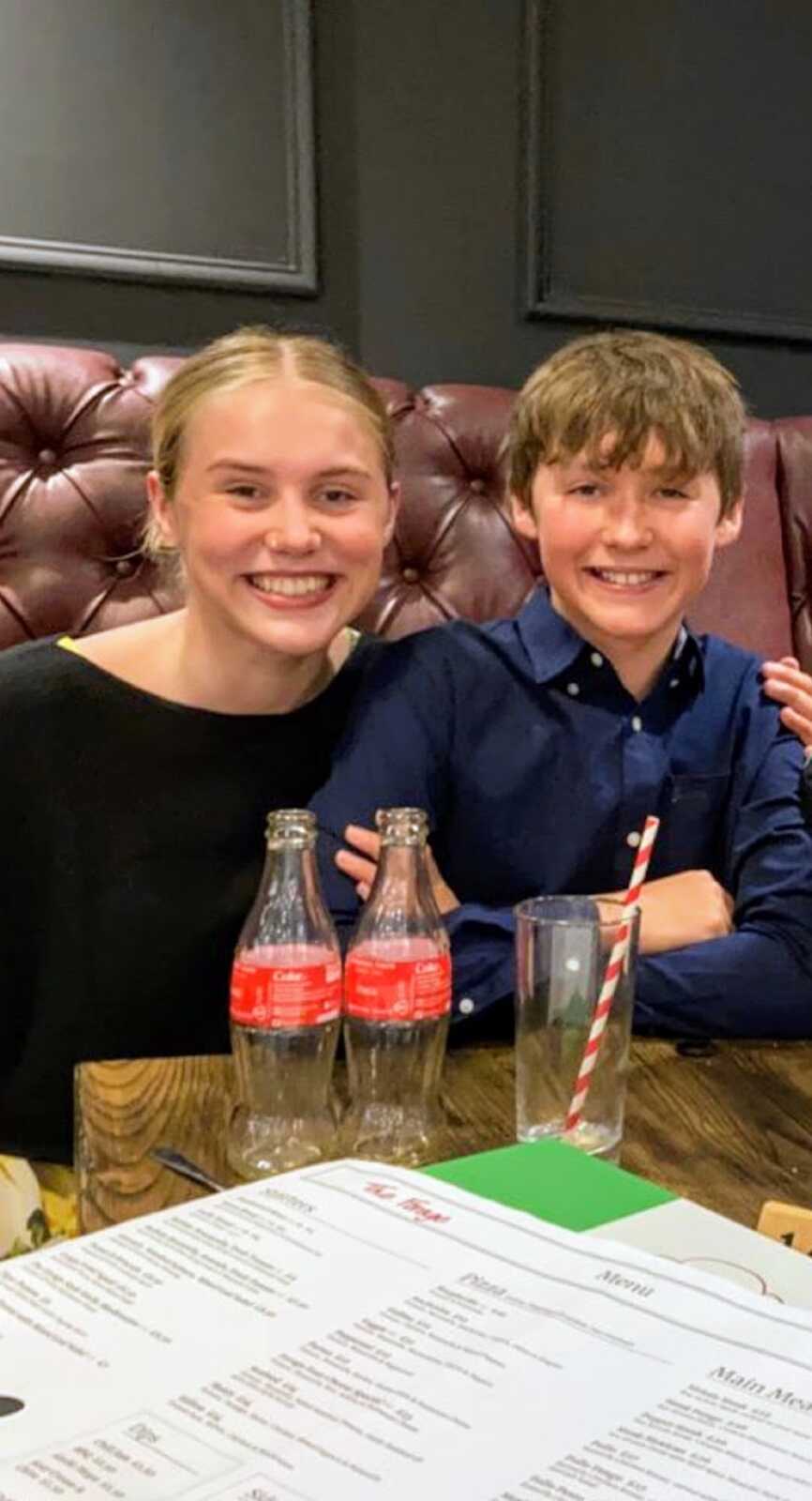 girl sitting in restaurant booth with younger brother