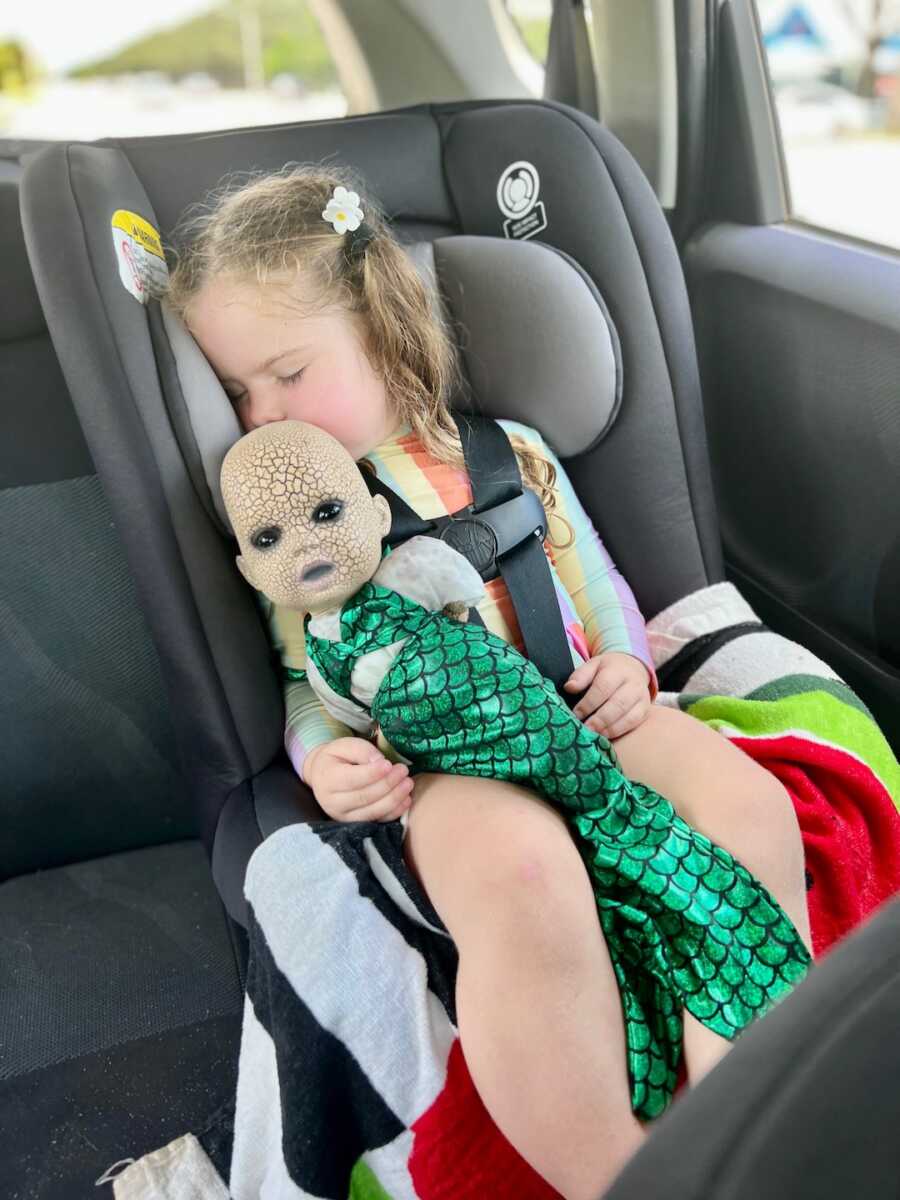 girl asleep in car with creepy halloween doll