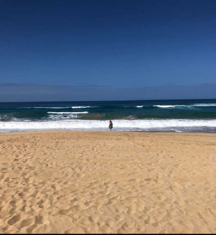 Grieving mom stands near the waves alone on the beach.