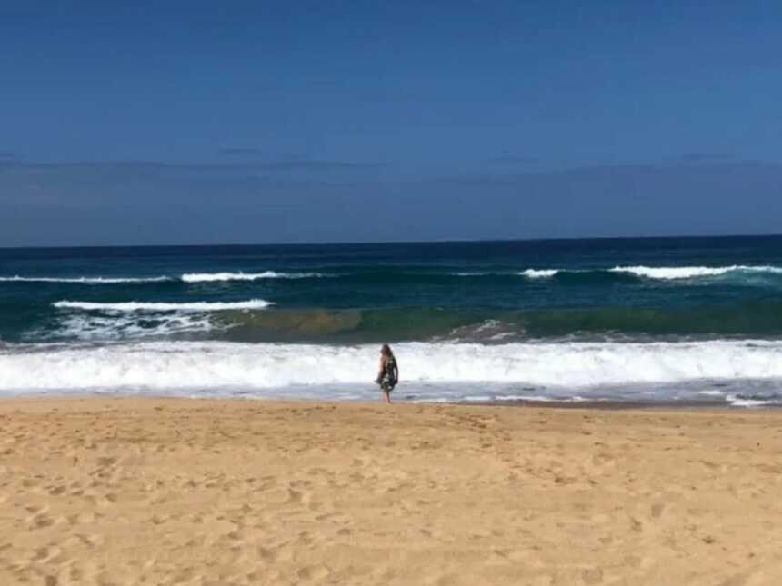 Grieving mom stands near the waves alone on the beach.