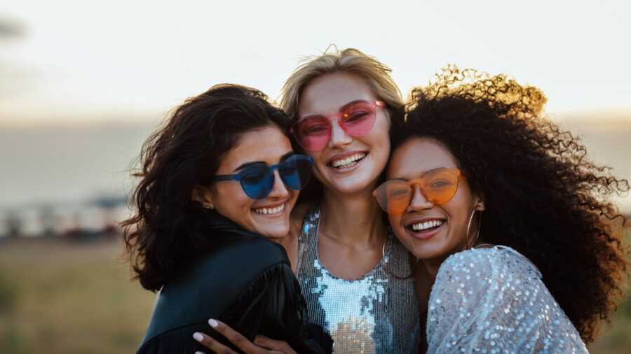 adult women wearing sunglasses hug and smile