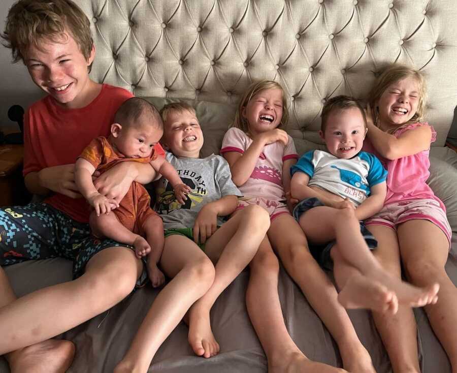 six siblings lie next to each other on bed laughing
