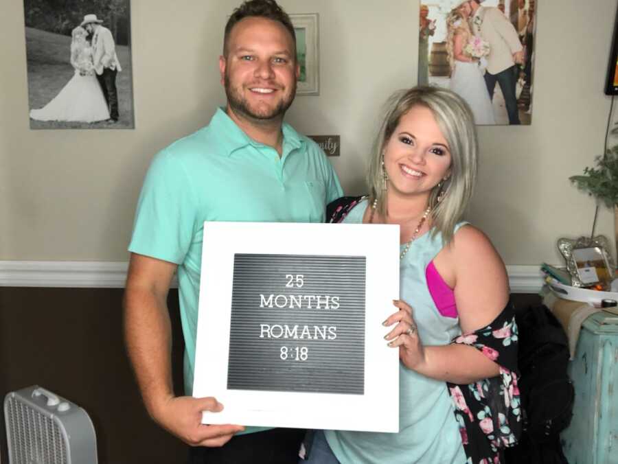 husband and wife holding sign stating 25 month infertility journey