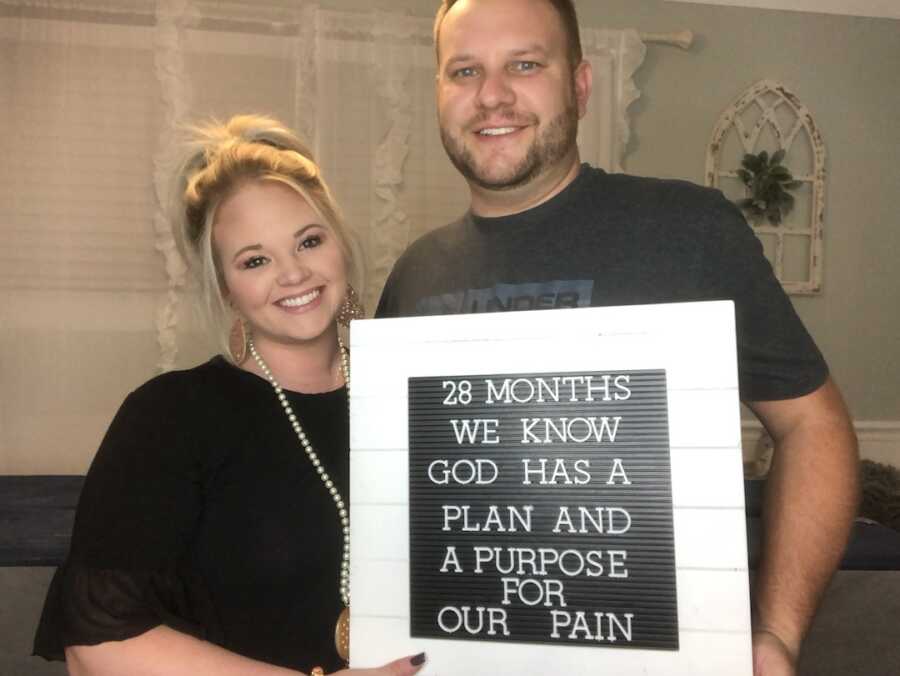 husband and wife with sign showing 28 month infertility battle