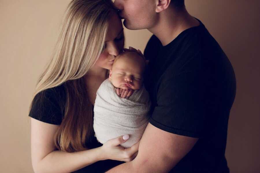 husband kissing wife's forehead who is kissing baby