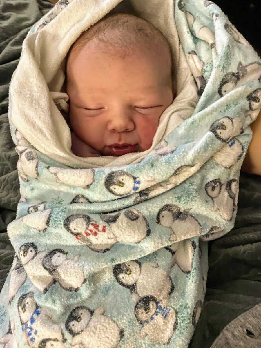 infant baby boy swaddled in a penguin blanket