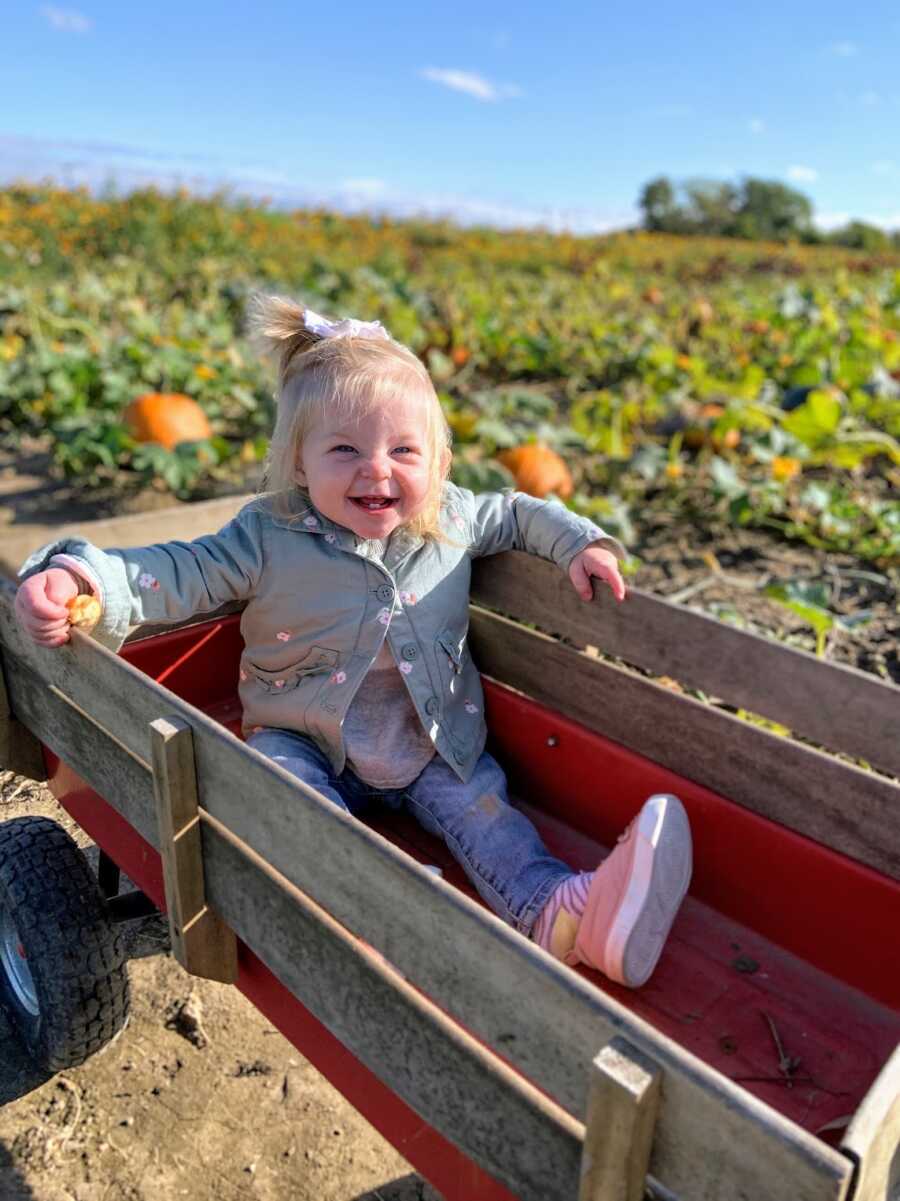 infant daughter sitting in wagon in a pumpkin patch and smiling