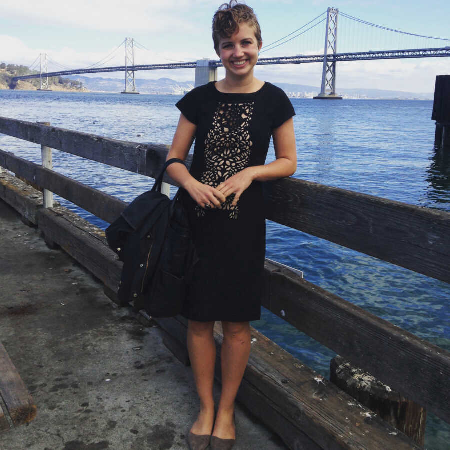 A young woman stands in front of water and a bridge