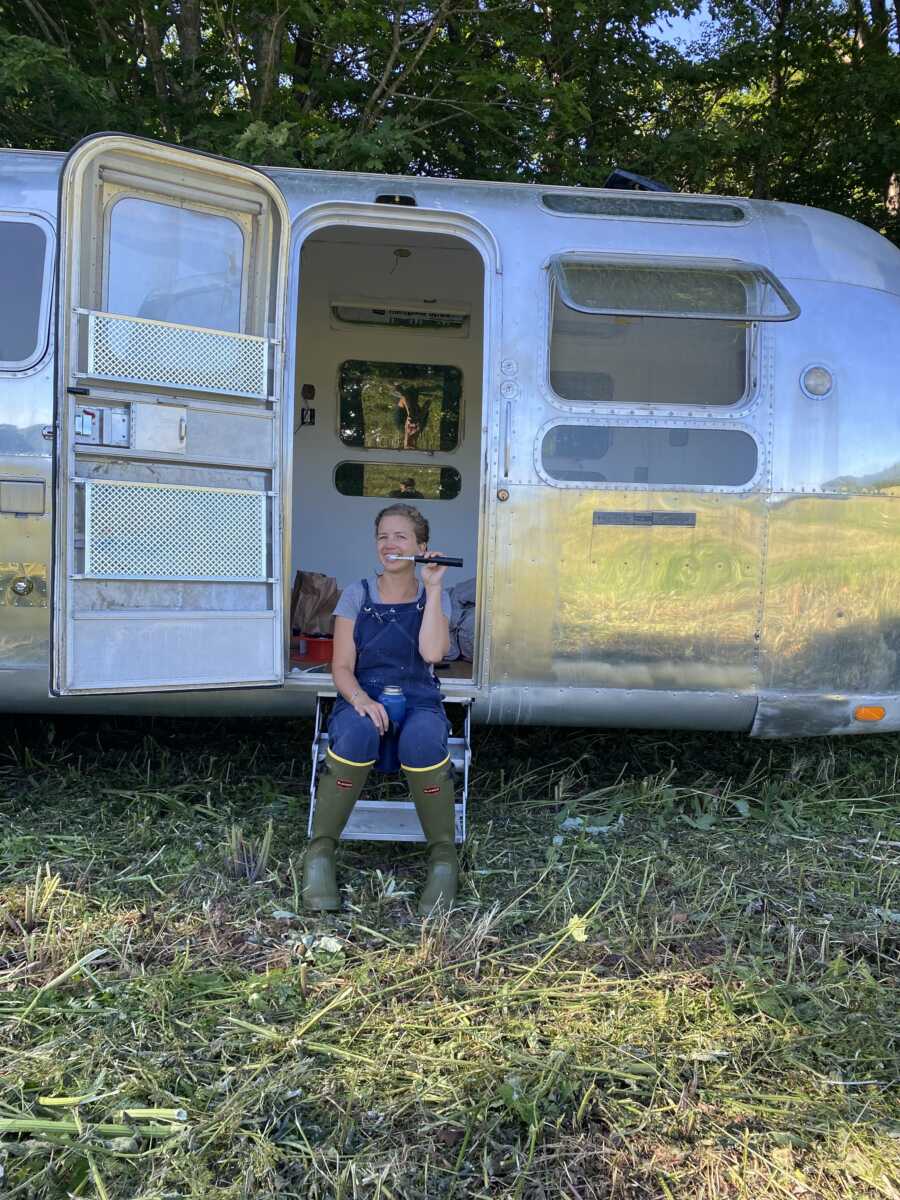 Woman brushes her teeth in farm gear outside her airstream trailer