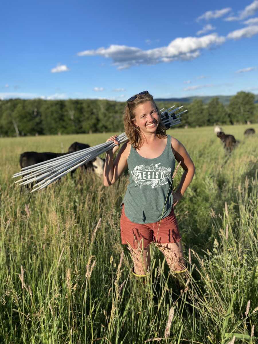 A woman stands with stakes on her farm with cows