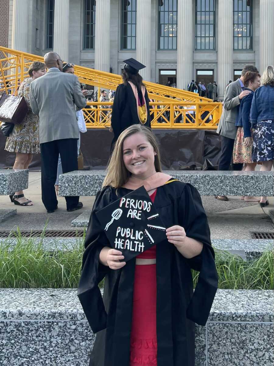Period educator at masters graduation poses with cap saying 'periods are public health'