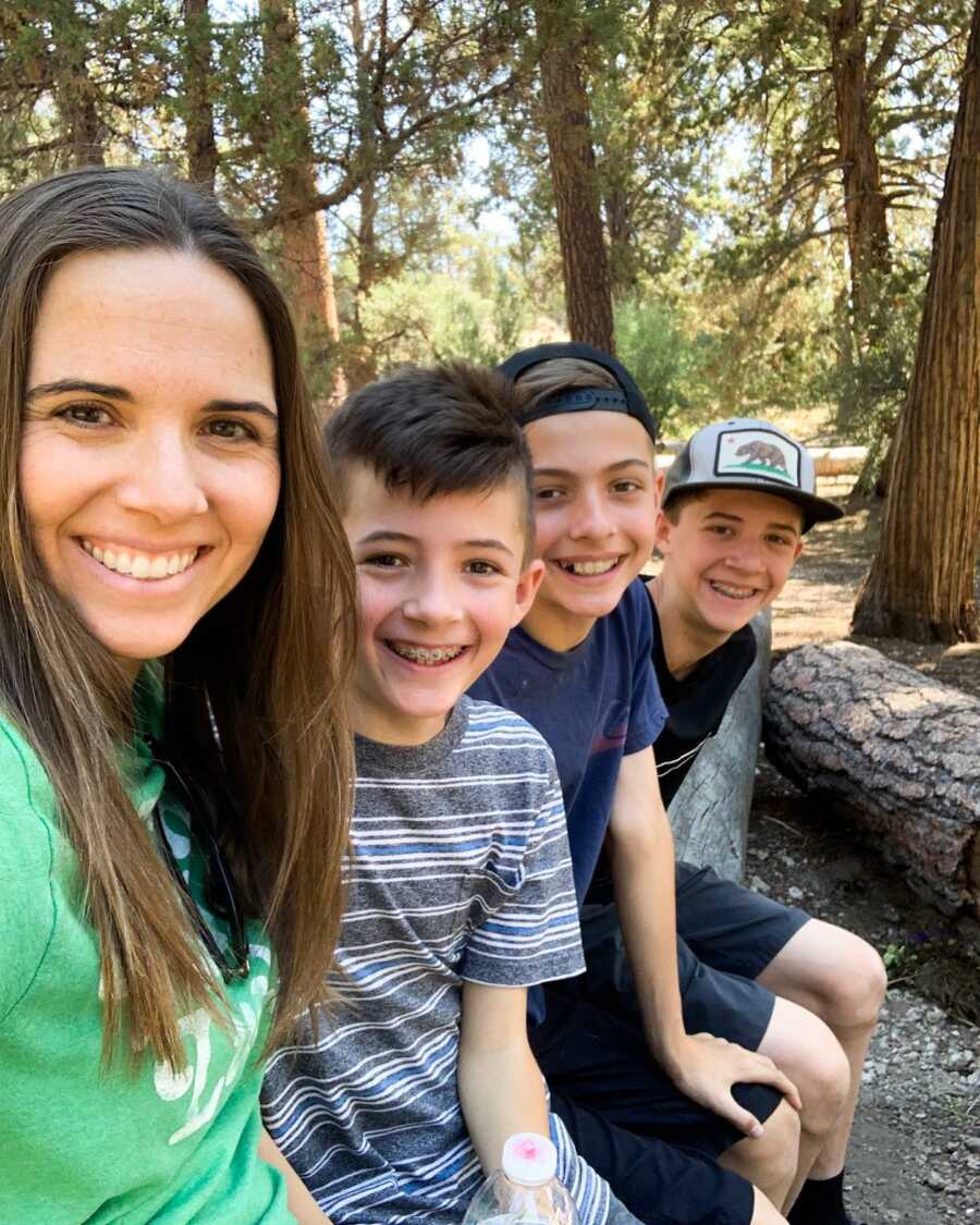 Mom sits next to her three boys on a fallen tree along their hiking path in California.