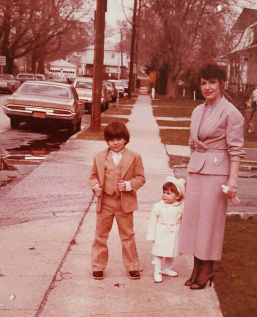 mom standing on sidewalk with her two children