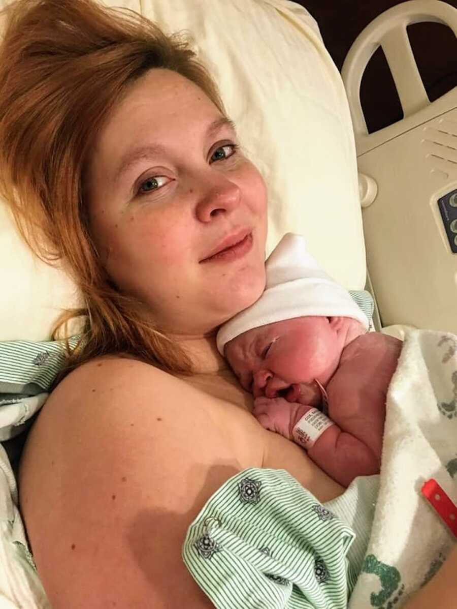 mother holding newborn rainbow baby girl in hospital bed