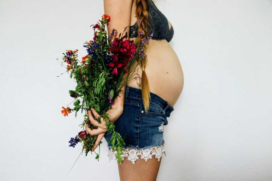 pregnant mother showing pregnancy belly and holding flowers