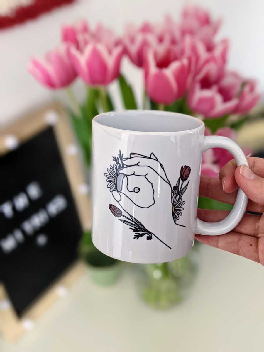 mug with a design of a hand holding a hearing aid and flowers