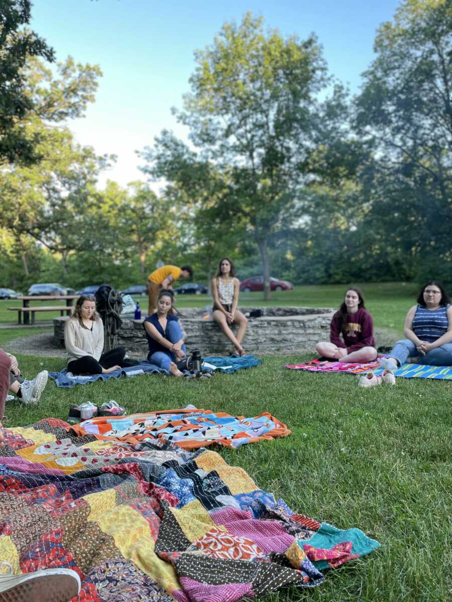 People at a period education bonfire sit on blankets 