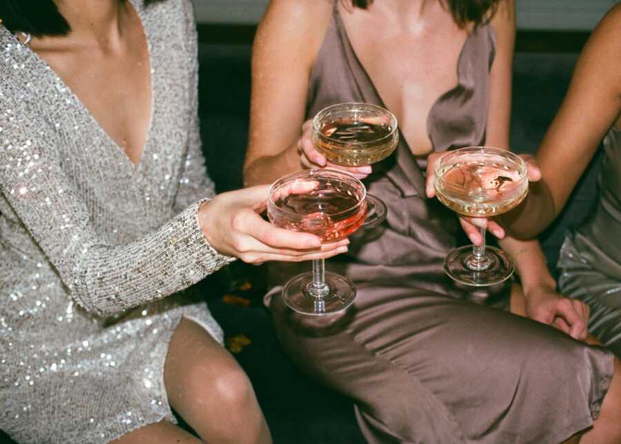 Three girls in evening gowns saying cheers with alcoholic drinks