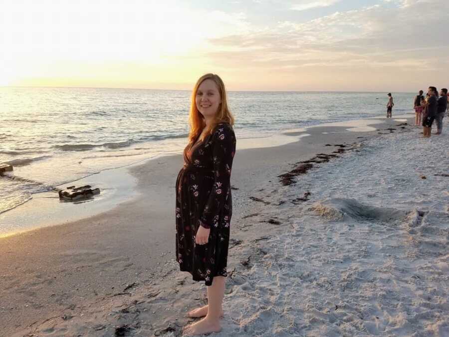 pregnant woman with PCOS standing on beach at sunset
