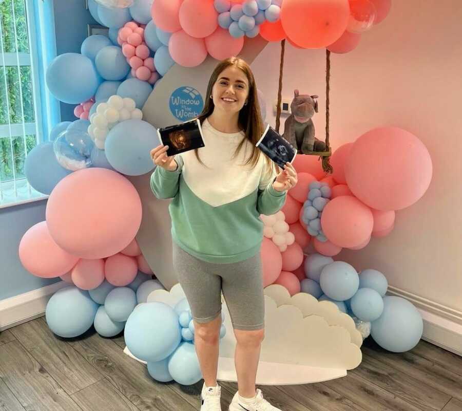 pregnant woman holding ultrasound photo infant of a pink and blue balloon moon