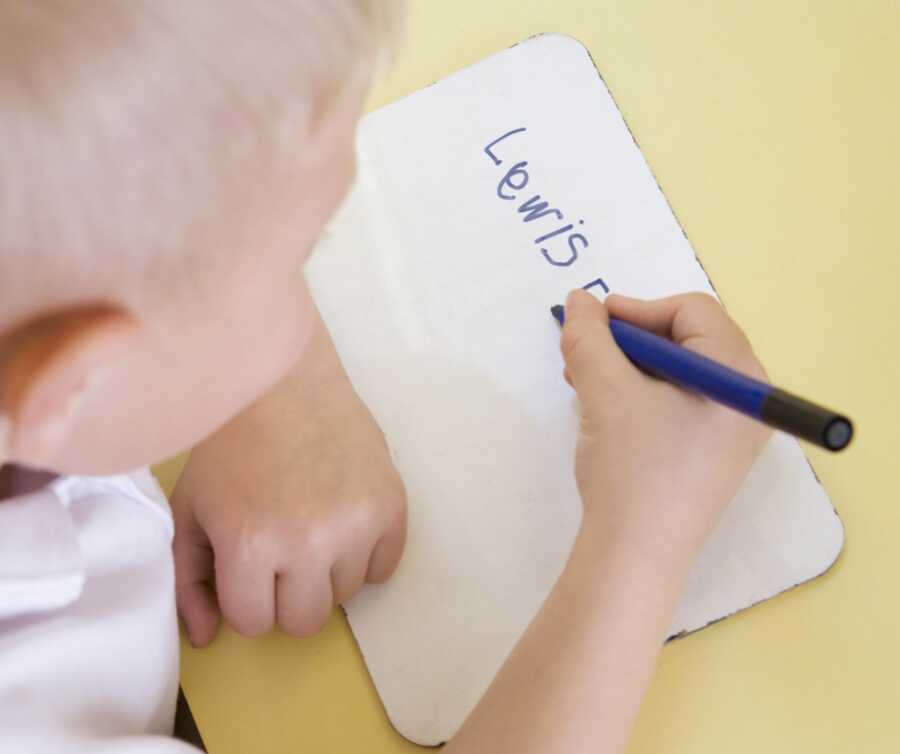 Young preschool boy sits at table and practices writing his name by himself.