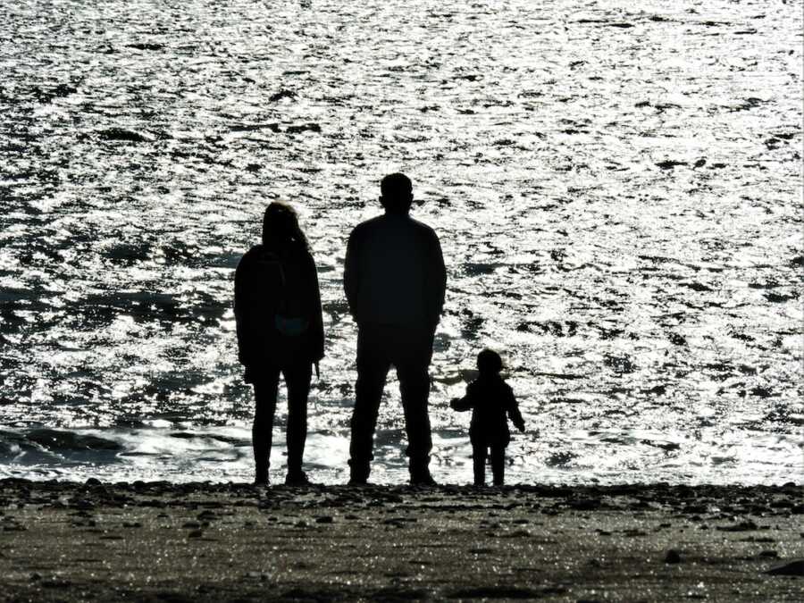 mom and dad coparenting toddler in front of beach waves