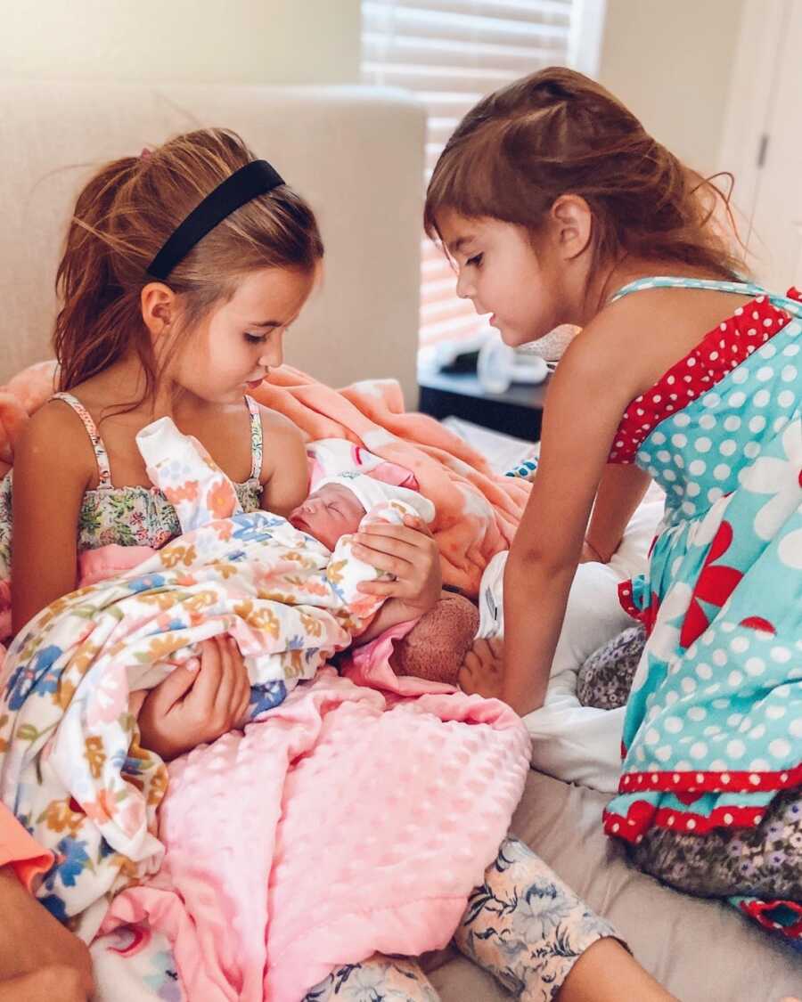 two big sisters sit admiring their little sister