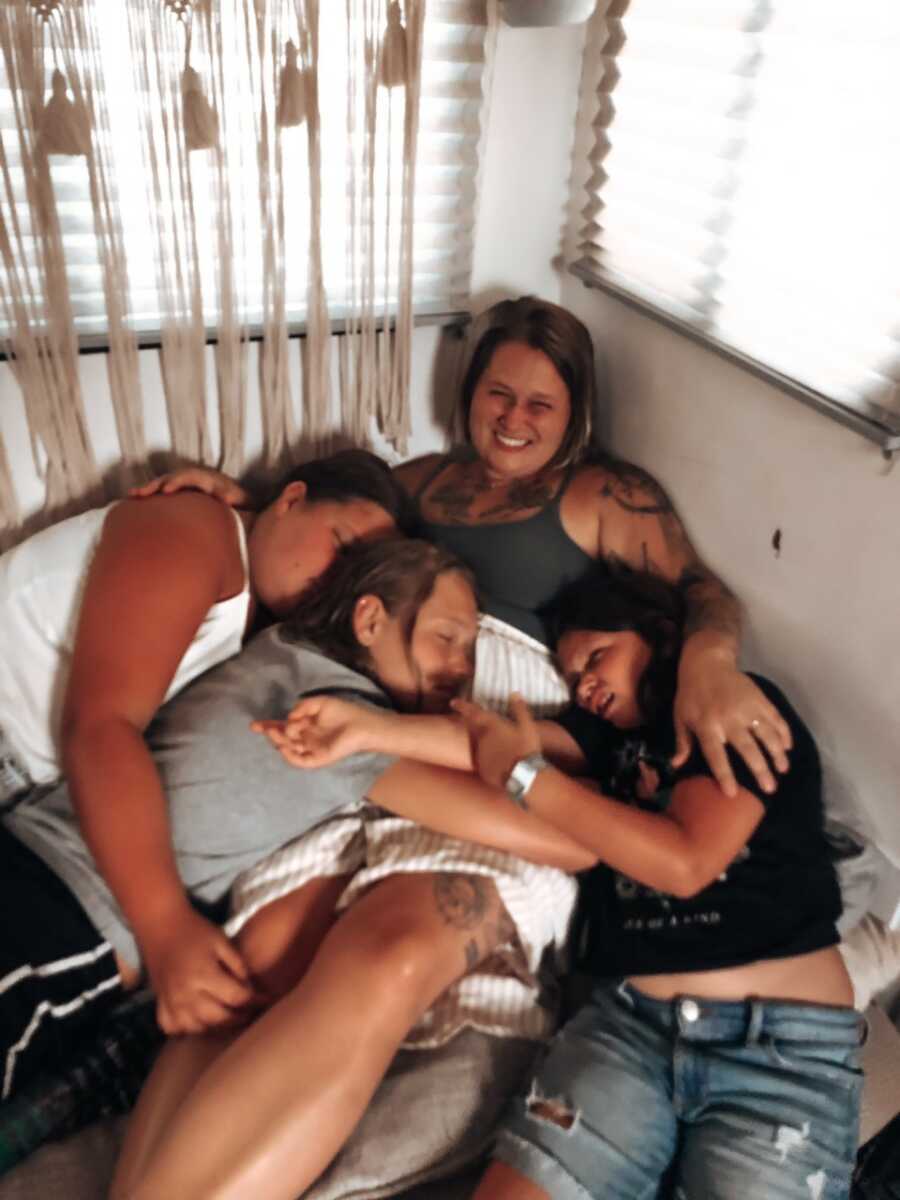 Daughters sleepily snuggle their mom lying on the bed in the corner of their home.