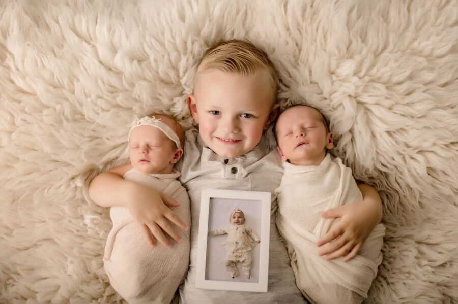 toddler boy holding his baby twin siblings and photo of his dead sister