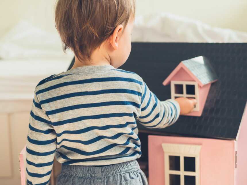 Toddler boy plays with pink dollhouse.