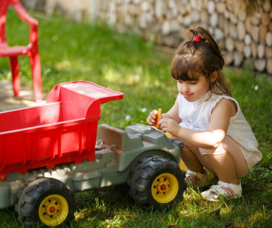 Little girl plays outside with a red dump truck.