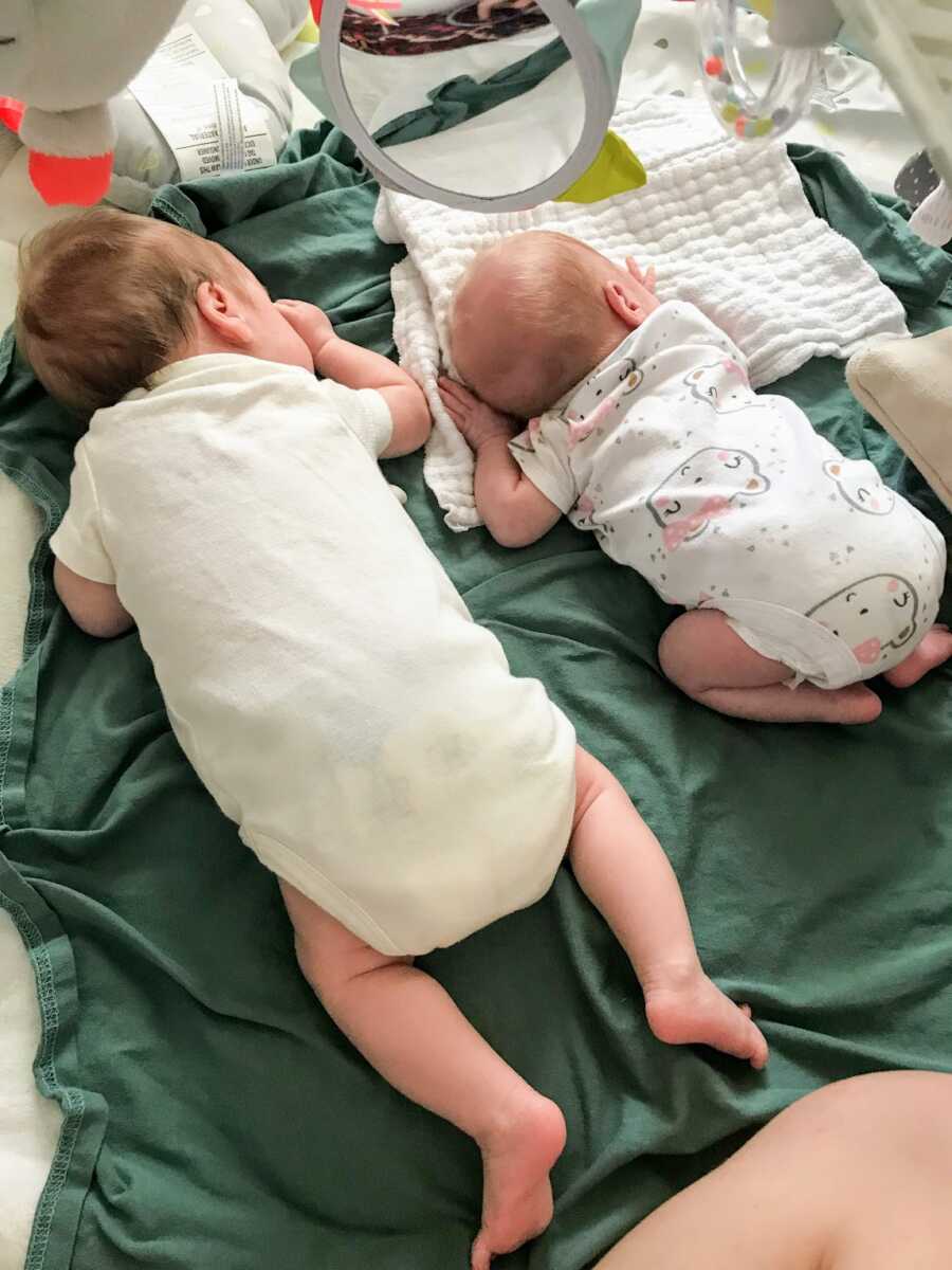 twin girls who are different sizes on a green blanket