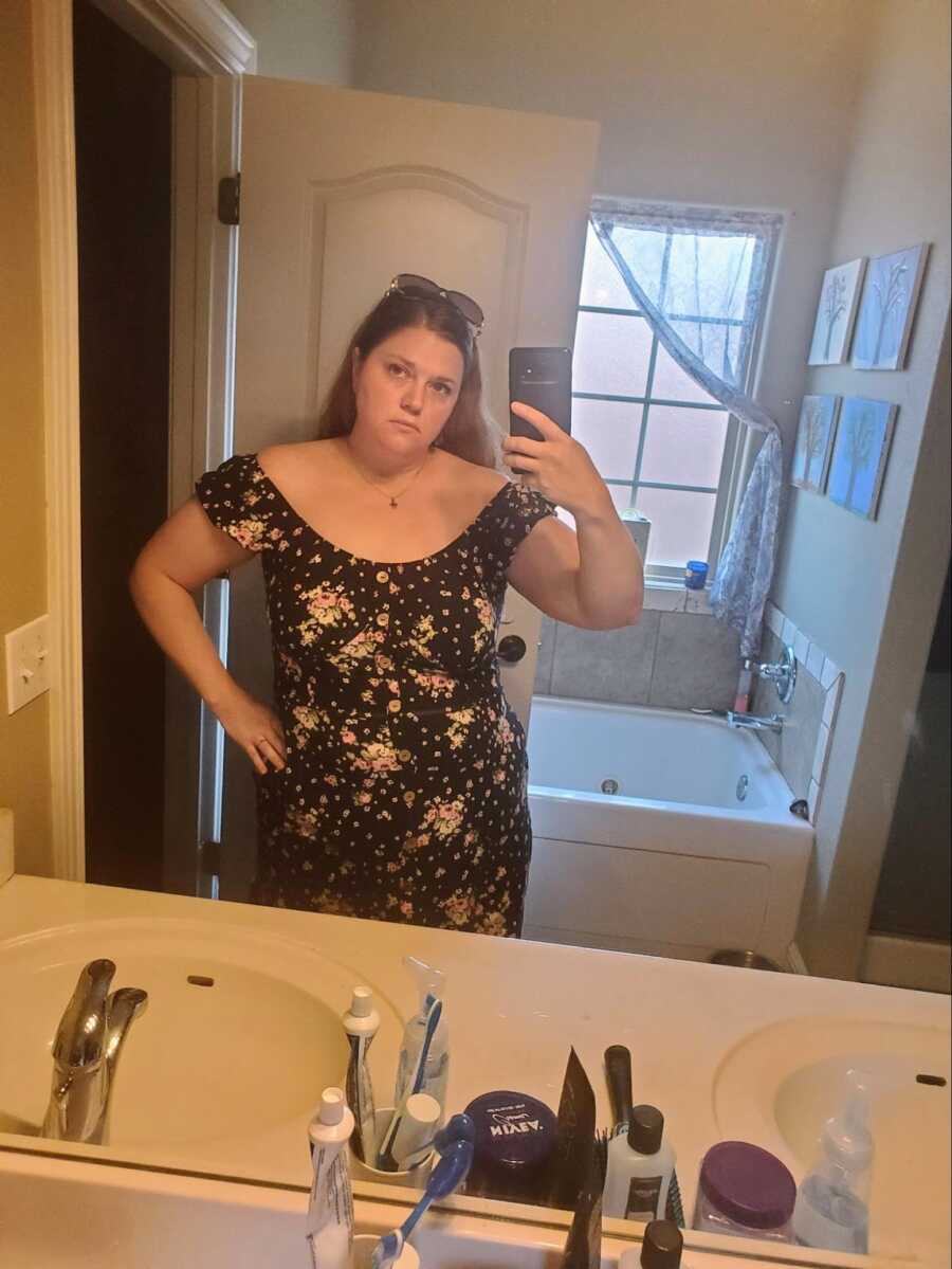 woman in black floral dress standing in front of bathroom mirror