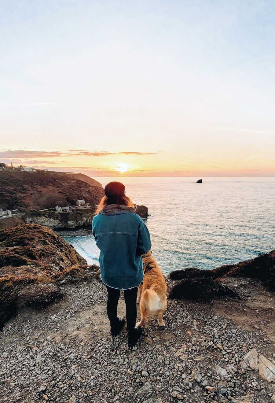 woman standing with dog at cliff overlook of ocean