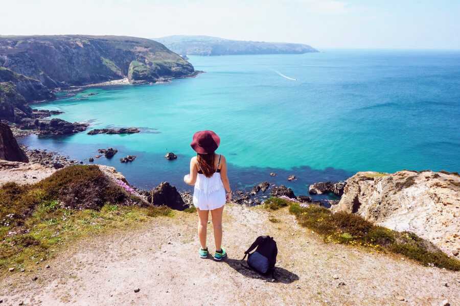 woman in white dress looking out over cliff edge at ocean