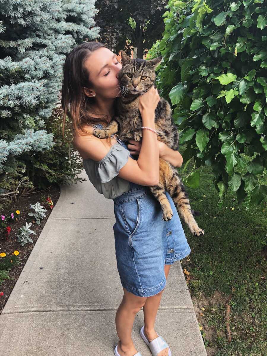 woman gives cat a kiss while holding them