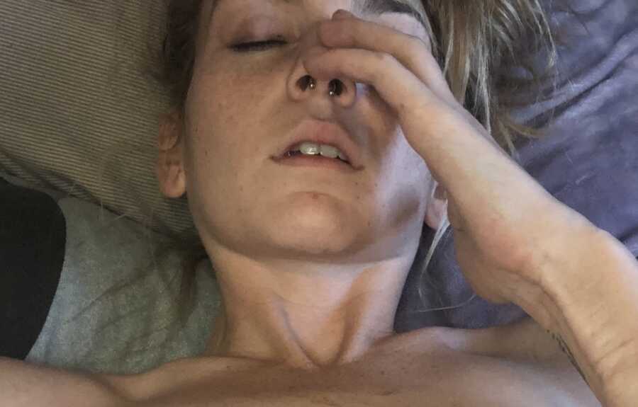 woman laying in bed with hand to nose, in pain