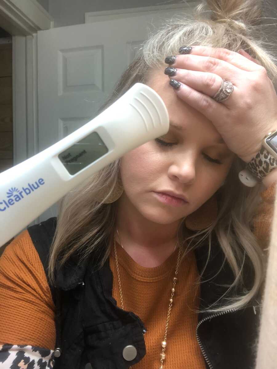woman holding head with negative pregnancy test