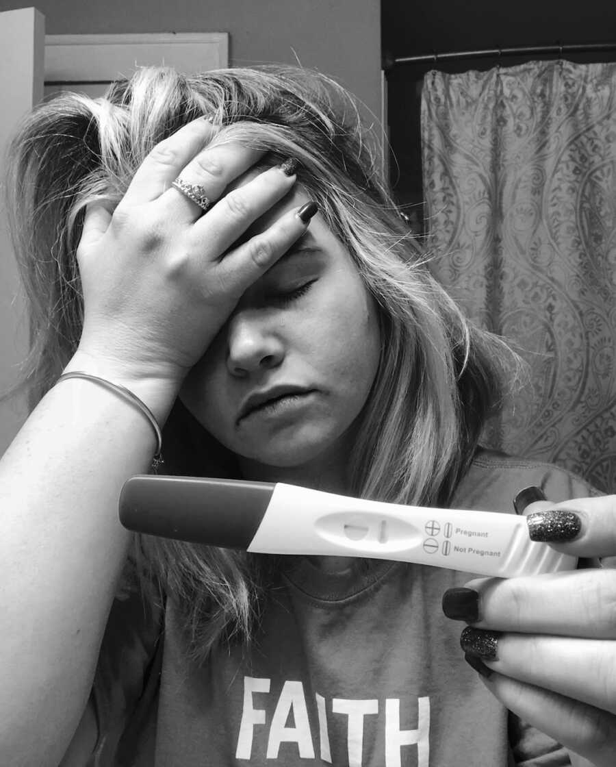 woman holds head with negative pregnancy test